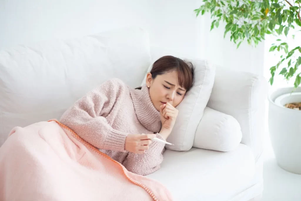 発熱外来。体温計を見てせき込む女性。